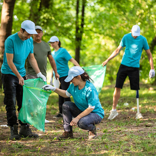 A team of 5 people in an open space environment surrounded by trees wearing gardening gloves picking up garden waste and placing in garden waste bags